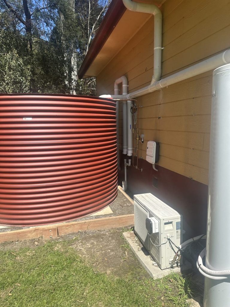A large red corrugated rainwater tank installed beside the Puffing Billy Railway building, with new downpipes, fittings and a control box on the wall.